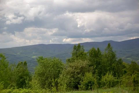 Dramatic cloudy skies over lush green mountains and tree covered hillsides. Stock Photos