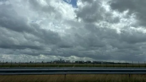 Dramatic cloudy sky above airport runway and distant terminal buildings, seen 库存照片