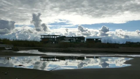 Dramatic cloudy sky over abandoned seaside buildings, mirrored in still water Stock Footage 317911064