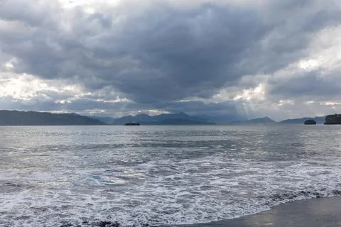 Dramatic cloudy sky over calm ocean waters and distant mountains Photos
