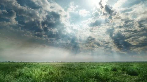 Dramatic cloudy sky over green field with sun rays Foto stock