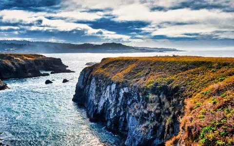 Dramatic cloudy sky over rugged coastal cliffs and ocean waves Stock Photos