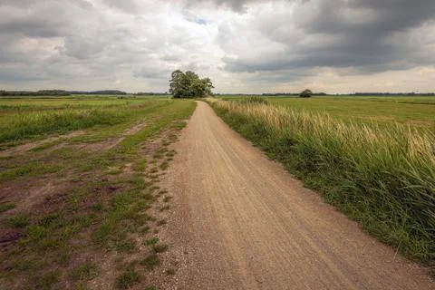 Dramatic cloudy sky over a winding gravel road in a rural landscape Stock Photos