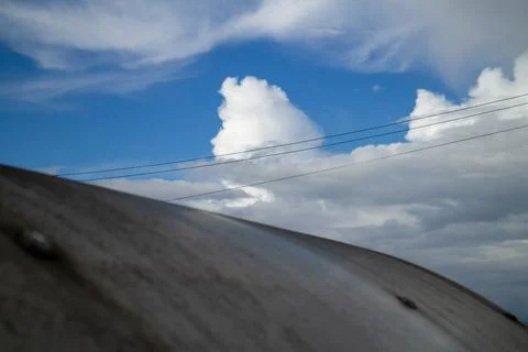 Dramatic cloudy sky with power lines passing across a curved industrial roof Stock Photos