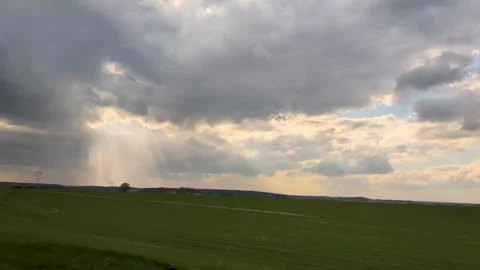 Dramatic cloudy sky with sun rays breaking through over a green field lands Stock Footage 308784881