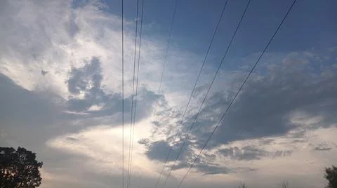 Dramatic cloudy sky at sunset with power lines and silhouette trees Stock Photos