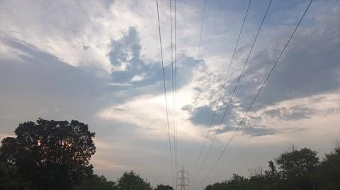 Dramatic cloudy sky at sunset with power lines and silhouette trees Stock Photos