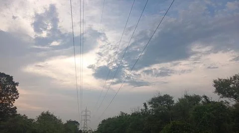 Dramatic cloudy sky at sunset with power lines and silhouette trees Stock Photos