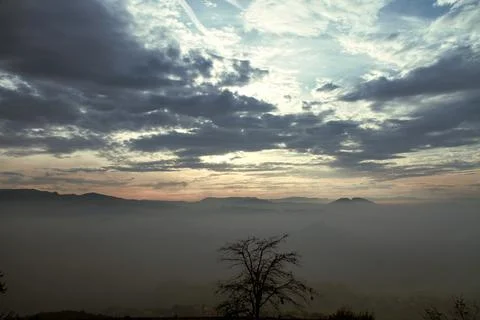 Dramatic cloudy sunrise over mountain landscape with tree silhouette. Stock Photos