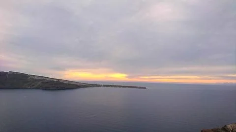 Dramatic cloudy sunset over the tranquil Aegean Sea and volcanic caldera cliffs Stock Photos