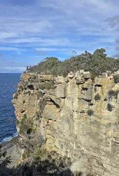 Dramatic coastal cliffs meet the deep blue ocean under a partly cloudy sky Stock Photos