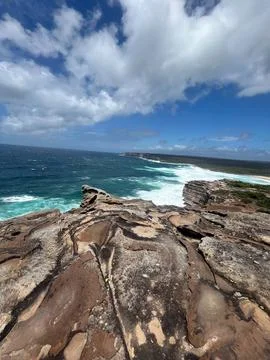 Dramatic coastal cliffs meet turquoise ocean waves under a cloudy blue sky Foto stock