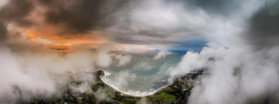 Dramatic coastal clouds obscure a serene ocean bay and residential area Foto stock