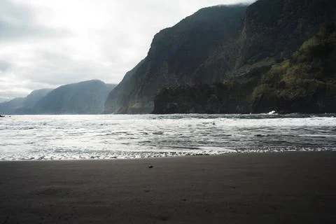 Dramatic Coastal Landscape with Dark Sand Beach and Rolling Waves Against T.. Stock Photos