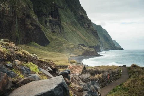 Dramatic coastal landscape with green cliffs, ocean waves, and a remote pat.. Stock Photos