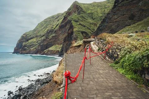 Dramatic Coastal Path with Red Rope Barrier Along Rugged Green Cliffs and B.. Stock Photos