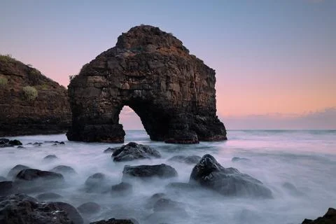 Dramatic coastal scene featuring a natural rock arch surrounded by ocean wave Stock Photos