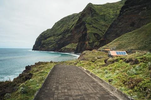 Dramatic coastal scene featuring an ocean, a small house with solar panels, a Stock Photos