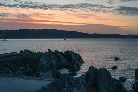Dramatic Coastal Sunrise Over Dark Rocky Shoreline and Calm Water Stock Photos