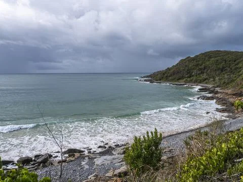 Dramatic coastal view featuring rocky beach, turquoise sea, and overcast sky Stock Photos