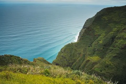 Dramatic Coastal View: Green Cliffs Meet Azure Ocean Waters with Rolling Wa.. Stock Photos