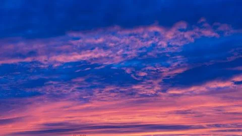 Dramatic colorful sunset clouds glowing across deep blue evening sky Stock Photos