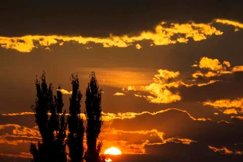 Dramatic colourful cloud formations with orange sun at sunset and silhouette of Stock Photos