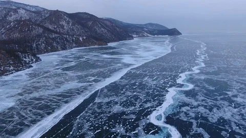 Dramatic cracks texture Lake Baikal coast Transparent blue ice Mountains Drone Stock Footage 87831207