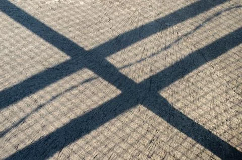 Dramatic crisscrossing shadows from a structure fall upon a textured concre.. Stock-Fotos