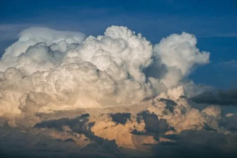 Dramatic cumulonimbus clouds glowing orange-white against deep blue sky Stock Photos