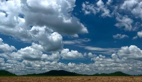 Dramatic cumulus clouds and blue sky over a barren field and distant hills. Stock Photos