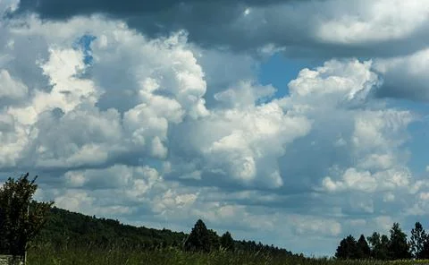 Dramatic cumulus clouds fill the sky above a green forested hill and grassy.. 스톡 사진