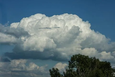 Dramatic cumulus clouds fill the sky above a lush green forest canopy 스톡 사진