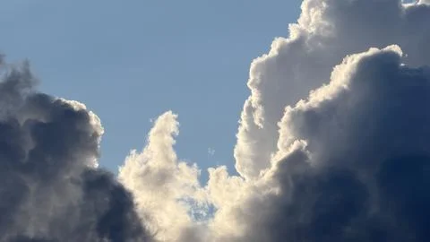Dramatic cumulus clouds with glowing sunlit edges against a clear blue sky Stock Photos