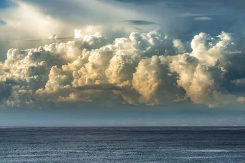 Dramatic cumulus clouds illuminated by golden sunlight over a dark ocean ho.. 写真素材