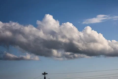 Dramatic cumulus clouds stretch across a bright blue sky with power lines bel Stock Photos