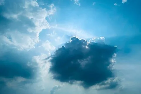 Dramatic dark cloud illuminated by sunbeams in a bright blue sky Stock Photos