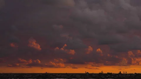 Dramatic dark clouds glow orange above silhouetted shoreline figures during Stock Footage 346277201