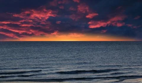 Dramatic dark red and yellow cloudy sky over blue sea with waves Stock Photos