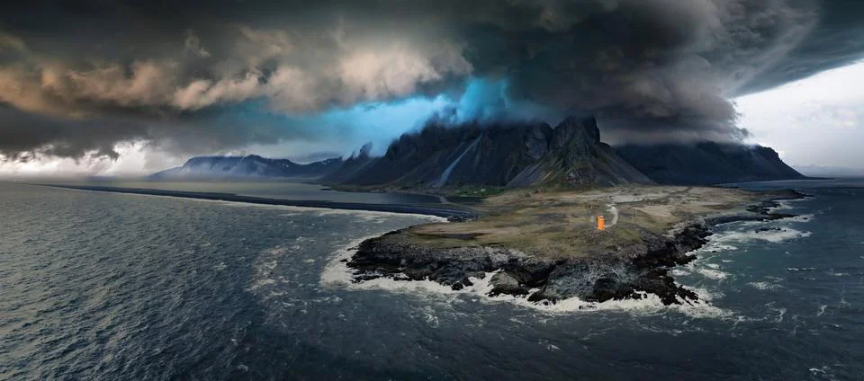 Dramatic Dark Sky Over Rugged Rocky Coastline with Orange Structure in Distance 스톡 사진