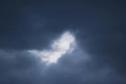 Dramatic dark storm cloud background with light glowing through a center gap 스톡 사진
