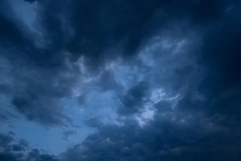 Dramatic dark storm clouds dominate a moody blue sky at dusk, natural backg.. Stock Photos