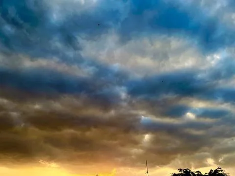 Dramatic dark storm clouds filling the sky with a warm golden orange sunset glow Stock Photos
