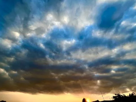 Dramatic dark storm clouds filling the sky with a warm golden orange sunset Stock Photos