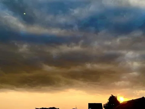 Dramatic dark storm clouds filling the sky with a warm golden orange sunset Stock Photos