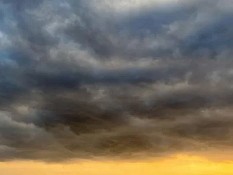 Dramatic dark storm clouds filling the sky with a warm golden orange sunset Stock Photos