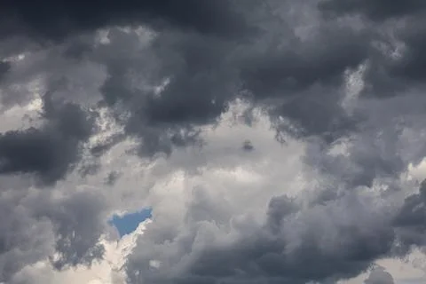 Dramatic dark storm clouds gather in the sky with a small patch of blue visib Stock Photos
