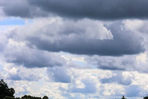 Dramatic dark storm clouds gather over a bright blue sky with scattered birds Stock Photos