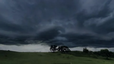 Dramatic dark storm clouds gathering over a vast rolling green grassy landscape Видео 347038427