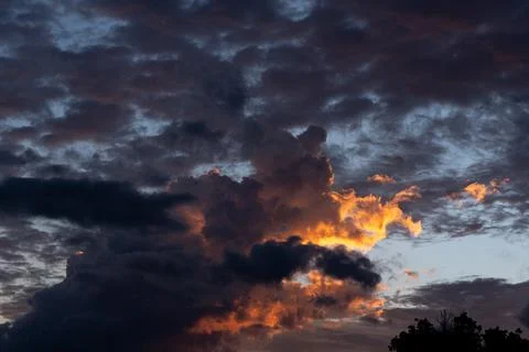 Dramatic dark storm clouds illuminated by golden sunset light 스톡 사진